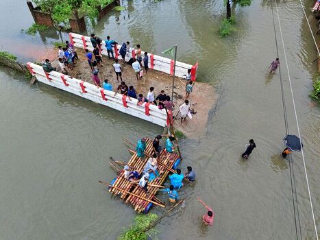 Banshkhali Upazila Chittagong Division Bangladesh 10 July 2026 Aerial view of a flooded area with people on a partially submerged bridge and a makeshift bamboo raft in the water. Banshkhali Upazila Chittagong Division Bangladesh 10 July 2026 Aerial view of a flooded area with people on a partially submerged bridge and a makeshift bamboo raft in the water.