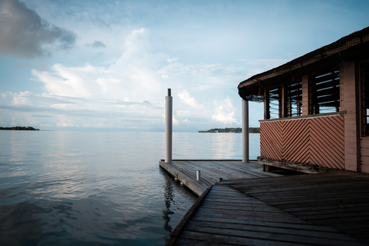 View of a wooden dock stretching into the calm reflective waters towards distant islands beneath a cloudy sky highlighting the stillness of the sea Gizo Gizo Solomon Island. View of a wooden dock stretching into the calm reflective waters towards distant islands beneath a cloudy sky highlighting the stillness of the sea Gizo Gizo Solomon Island.
