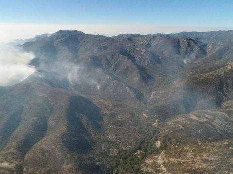 Aerial view of the Sierra de San Miguelito mountain range with smoke rising from a wildfire across the rugged dry landscape under a clear blue sky in San Luis Potosi San Luis Potosi Mexico.