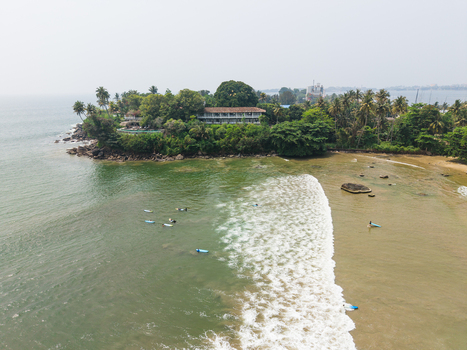 Aerial view of surfers in the ocean near Dewata Beach Road with breaking waves and lush tropical greenery in Galle Southern Province Sri Lanka.