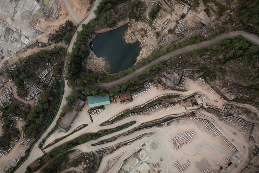 Aerial view of Cantera Porrino a granite quarry featuring deep water filled pits stacked stone blocks and winding access roads surrounded by forest in O Porrino Pontevedra Spain. Aerial view of Cantera Porrino a granite quarry featuring deep water filled pits stacked stone blocks and winding access roads surrounded by forest in O Porrino Pontevedra Spain.