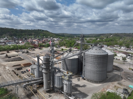 Aerial view of large industrial grain silos and metal storage bins with a small town and green hills under a cloudy sky in Aurora Indiana United States. Aerial view of large industrial grain silos and metal storage bins with a small town and green hills under a cloudy sky in Aurora Indiana United States.