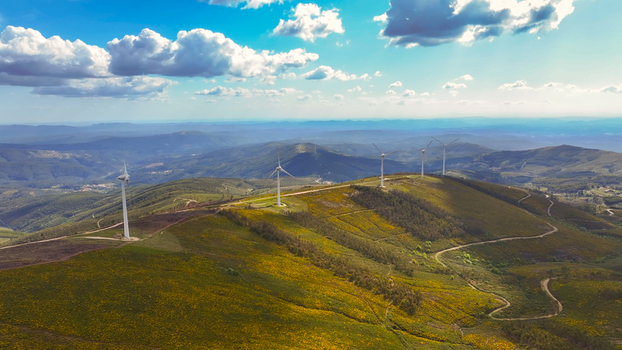Aerial view of wind turbines standing on rolling hills covered in green and yellow vegetation with winding dirt roads under a bright blue sky in Lisbon Lisbon Portugal. Aerial view of wind turbines standing on rolling hills covered in green and yellow vegetation with winding dirt roads under a bright blue sky in Lisbon Lisbon Portugal.