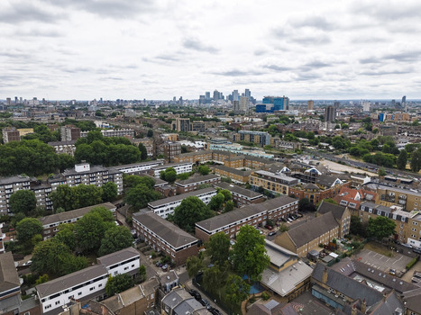Aerial view of Shoreditch featuring dense residential housing terraced brick buildings and lush green trees with the distant city skyline in London England United Kingdom. Aerial view of Shoreditch featuring dense residential housing terraced brick buildings and lush green trees with the distant city skyline in London England United Kingdom.