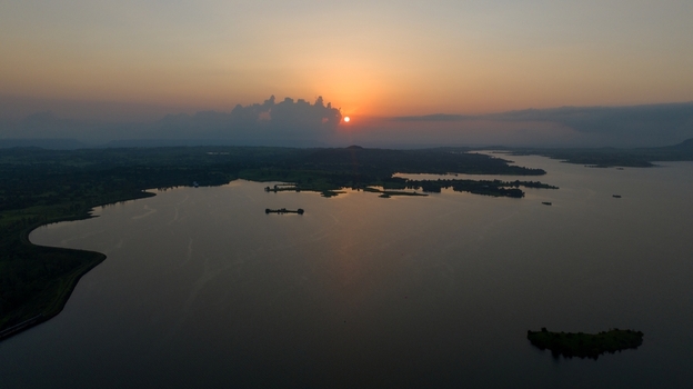 Aerial view of Upper Vaitarana Dam at sunset with calm reservoir waters surrounding hills and a golden sky in Ondli Maharashtra India.