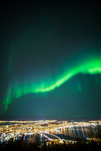 View of the northern lights illuminating the night sky above the city lights and bridge of Tromso Troms Norway. View of the northern lights illuminating the night sky above the city lights and bridge of Tromso Troms Norway.