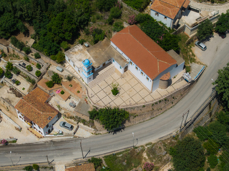 Aerial view of a traditional Orthodox church with a blue domed bell tower and a paved courtyard surrounded by lush greenery and a winding road in Dhermi Vlore County Albania. Aerial view of a traditional Orthodox church with a blue domed bell tower and a paved courtyard surrounded by lush greenery and a winding road in Dhermi Vlore County Albania.