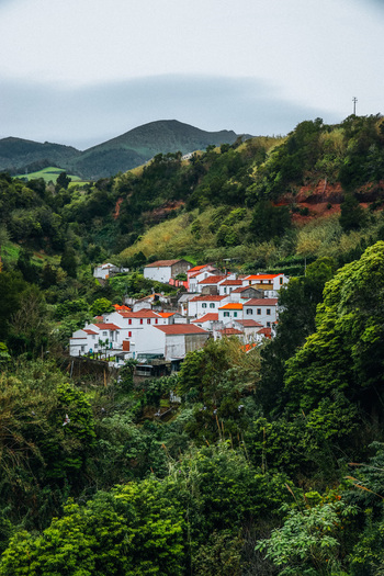View of the village nestles amid lush green vegetation with white houses and red roofs contrasting with the surrounding mountains Furnas Azores Portugal.
