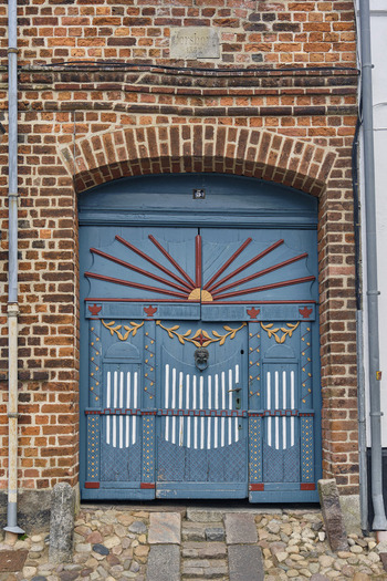 Ribe Denmark 20 July 2026 View of an ornate blue wooden door with intricate carvings a sunburst motif and a lion head knocker set into a historic brick wall in the old town.