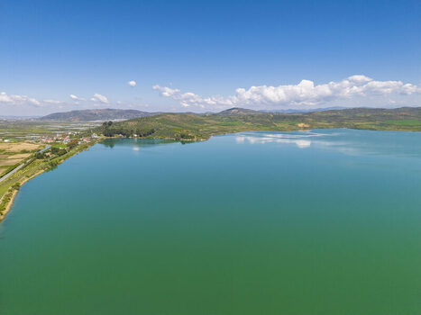 Aerial view of Liqeni Thanes turquoise lake surrounded by rolling hills green fields and a clear blue sky in Lushnje Fier County Albania. Aerial view of Liqeni Thanes turquoise lake surrounded by rolling hills green fields and a clear blue sky in Lushnje Fier County Albania.