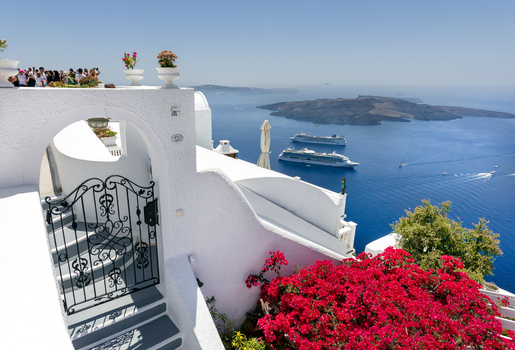 View of the iconic white architecture and arched gate adorned with vibrant red bougainvillea overlooking the caldera and cruise ships in the Aegean Sea in Fira Greece. View of the iconic white architecture and arched gate adorned with vibrant red bougainvillea overlooking the caldera and cruise ships in the Aegean Sea in Fira Greece.