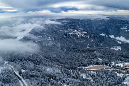 Aerial view of the snow covered Mummelsee area in the Black Forest with dense pine forests winding roads and low hanging clouds in Seebach Baden Wurttemberg Germany. Aerial view of the snow covered Mummelsee area in the Black Forest with dense pine forests winding roads and low hanging clouds in Seebach Baden Wurttemberg Germany.