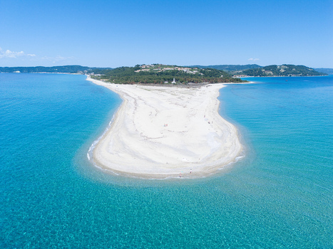 Aerial view of the white sand spit of Possidi Beach surrounded by turquoise crystal clear waters and green hills under a blue sky Greece.