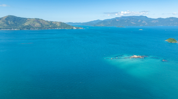 Aerial view of Ilha de Cataguas surrounded by turquoise waters and lush green mountains in the background in Angra dos Reis State of Rio de Janeiro Brazil.