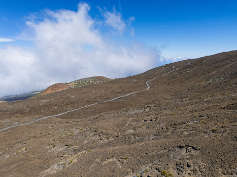 Aerial view of the winding road on the volcanic slopes of Mauna Kea under a blue sky with clouds in Hawaii County Hawaii United States.