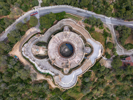Aerial view of the circular Castillo de Bellver with its unique Gothic architecture surrounded by lush green pine forests and a winding road in Palma Illes Balears Spain.