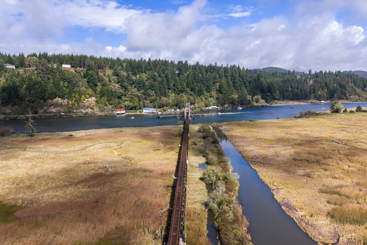 Aerial view of the Siuslaw River Train Bridge spanning the river surrounded by marshland dense forest and a blue sky in Florence Oregon United States.