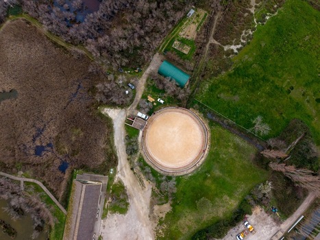 Aerial view of the Scamandre Regional Nature Reserve featuring a circular horse arena surrounded by lush green fields and marshlands in Arles Provence Alpes Cote d Azur France. Aerial view of the Scamandre Regional Nature Reserve featuring a circular horse arena surrounded by lush green fields and marshlands in Arles Provence Alpes Cote d Azur France.