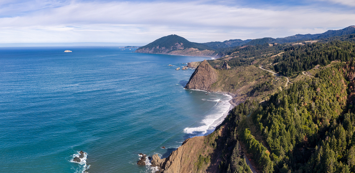 Aerial view of Highway 101 winding along the rugged cliffs and forested coastline of the Pacific Ocean in Port Orford Oregon United States. Aerial view of Highway 101 winding along the rugged cliffs and forested coastline of the Pacific Ocean in Port Orford Oregon United States.