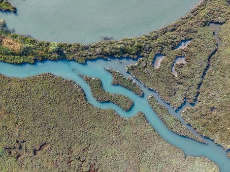 Aerial view of the winding turquoise waters of Kanali i Vivarit flowing through lush green marshland and textured wetlands in Vrine Vlore County Albania. Aerial view of the winding turquoise waters of Kanali i Vivarit flowing through lush green marshland and textured wetlands in Vrine Vlore County Albania.