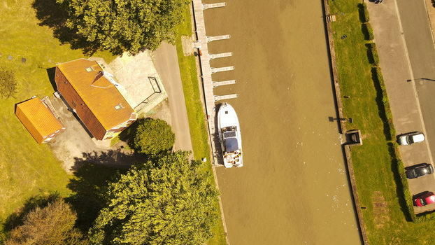 Aerial view of a boat docked at a pier along a canal next to a building with a tiled roof and parked cars in Saint Omer Hauts de France France. Aerial view of a boat docked at a pier along a canal next to a building with a tiled roof and parked cars in Saint Omer Hauts de France France.