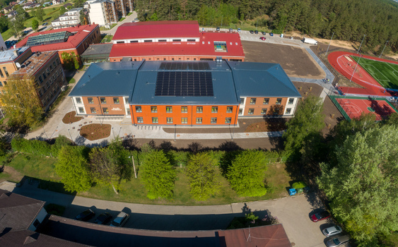 Aerial view of a modern school building with a red brick facade and solar panels on the roof featuring an adjacent sports field and running track in Latvia. Aerial view of a modern school building with a red brick facade and solar panels on the roof featuring an adjacent sports field and running track in Latvia.