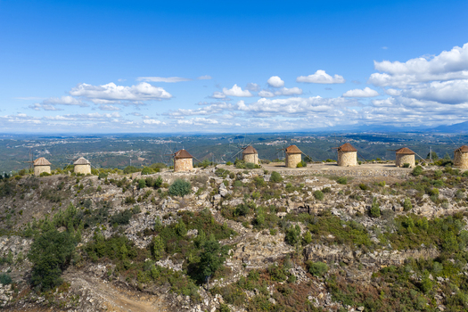 Aerial view of Moinhos da Serra da Atalhada a series of historic stone windmills situated on a rocky ridge under a clear blue sky in Penacova Coimbra Portugal.