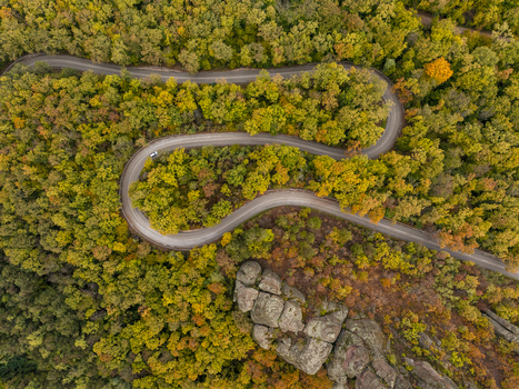 Aerial view of a winding road snaking through a dense autumn forest with vibrant yellow and orange foliage and the unique rock formations of Belogradchik in Belogradchik Vidin Bulgaria. Aerial view of a winding road snaking through a dense autumn forest with vibrant yellow and orange foliage and the unique rock formations of Belogradchik in Belogradchik Vidin Bulgaria.