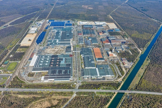 Aerial view of sprawling industrial buildings and solar panels contrasting against the surrounding green forests and a canal s blue waters Sausheim Grand Est France.