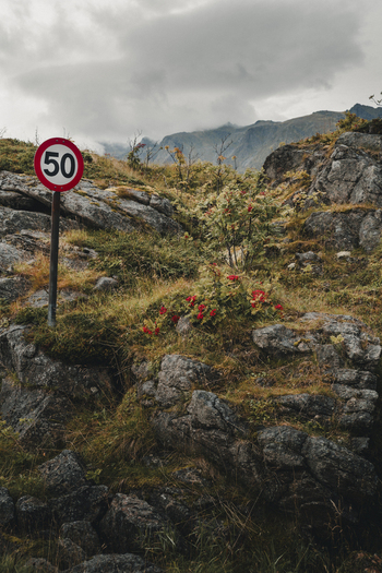 Sund Norway 04 September 2025 View of a speed limit sign standing in a rugged rocky landscape with sparse vegetation and mountains under a cloudy sky in Sund Nordland Norway.
