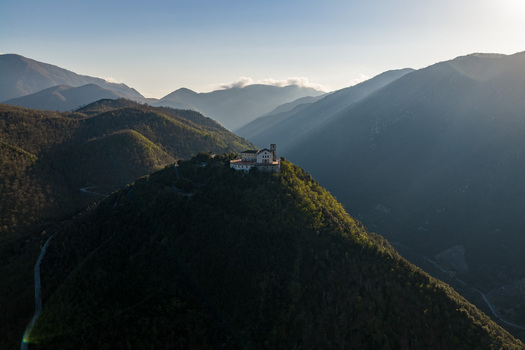 Aerial view of Santuario del Santissimo Salvatore atop a forested mountain peak surrounded by the Apennine mountains under soft sunlight rays Montella Campania Italy. Aerial view of Santuario del Santissimo Salvatore atop a forested mountain peak surrounded by the Apennine mountains under soft sunlight rays Montella Campania Italy.