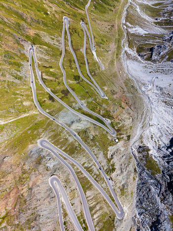 Aerial view of the winding hairpin turns of the Stelvio Pass mountain road surrounded by alpine meadows and rocky slopes in Stilfs Trentino Alto Adige Italy.