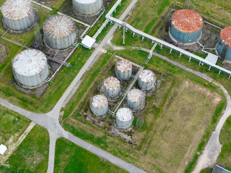 Aerial view of industrial storage tanks with rusty tops and connecting pipelines situated in a green field in Olaine parish Olaine Municipality Latvia.