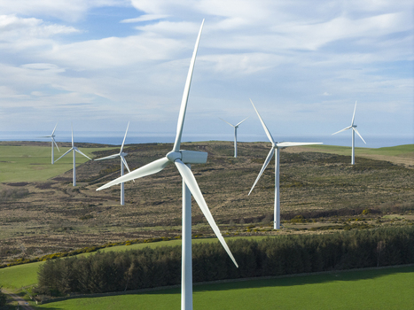 Aerial view of wind turbines standing on rolling hills with green fields and a distant sea horizon under a blue sky Scotland United Kingdom. Aerial view of wind turbines standing on rolling hills with green fields and a distant sea horizon under a blue sky Scotland United Kingdom.