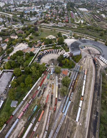 Aerial view of the Hungarian Railway Museum featuring a circular depot with numerous historic locomotives and train tracks surrounded by lush trees in Budapest Hungary. Aerial view of the Hungarian Railway Museum featuring a circular depot with numerous historic locomotives and train tracks surrounded by lush trees in Budapest Hungary.