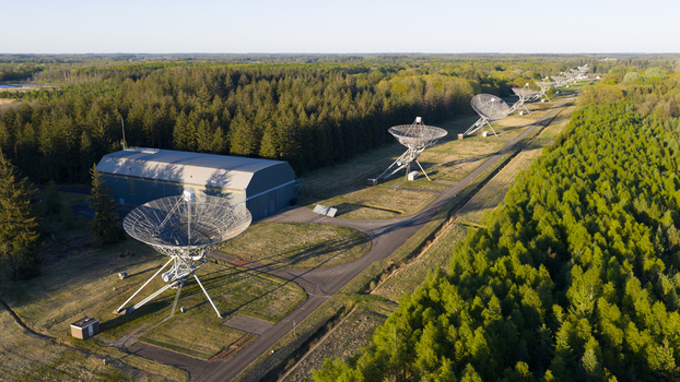 Aerial view of the large radio telescope dishes and a hangar building surrounded by dense green forest in Westerbork Drenthe Netherlands. Aerial view of the large radio telescope dishes and a hangar building surrounded by dense green forest in Westerbork Drenthe Netherlands.
