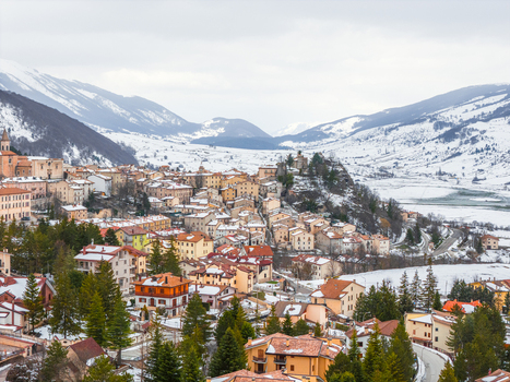 Aerial view of the historic town of Pescocostanzo nestled in snow covered mountains featuring stone buildings terracotta rooftops and evergreen trees in Pescocostanzo Abruzzo Italy.