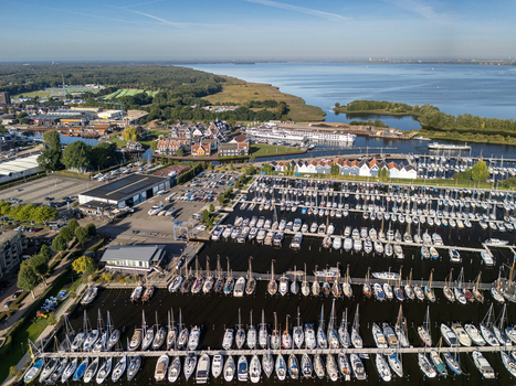 Aerial view of a large marina filled with numerous sailboats docked in rows surrounded by buildings and green landscape in Huizen North Holland Netherlands.