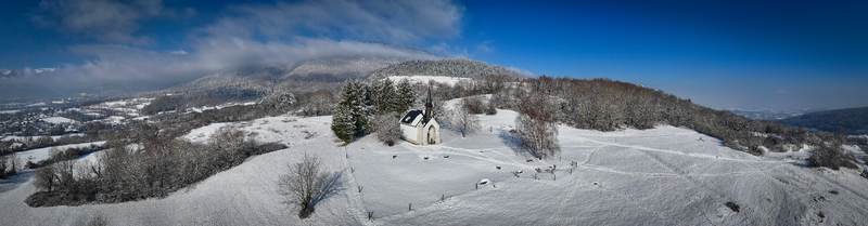 Aerial view of Chapelle Notre Dame de Riantmont on a snow covered hill surrounded by winter trees and misty mountains Vesancy Auvergne Rhone Alpes France.