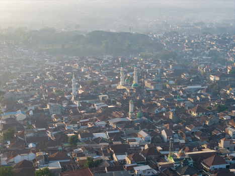 Aerial view of the dense urban landscape featuring prominent mosques with green domes and minarets amidst residential rooftops in the morning light in Malang East Java Indonesia.