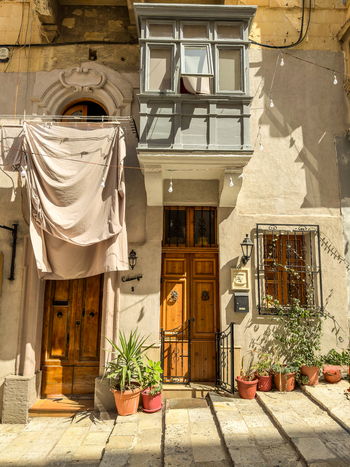 View of sun drenched architecture a weathered door flanked by potted plants and a draped cloth create a scene of everyday life Valletta Malta. View of sun drenched architecture a weathered door flanked by potted plants and a draped cloth create a scene of everyday life Valletta Malta.
