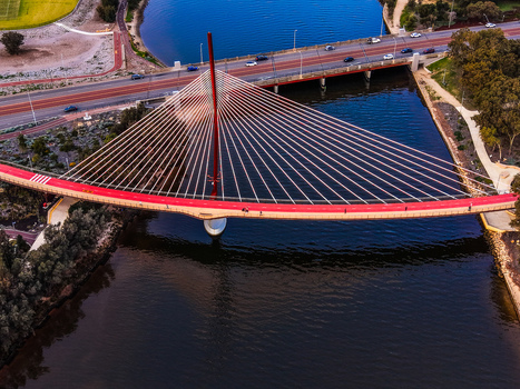 Aerial view of the red Boorloo Bridge spanning the Swan River with surrounding parkland and road infrastructure in East Perth Western Australia Australia.