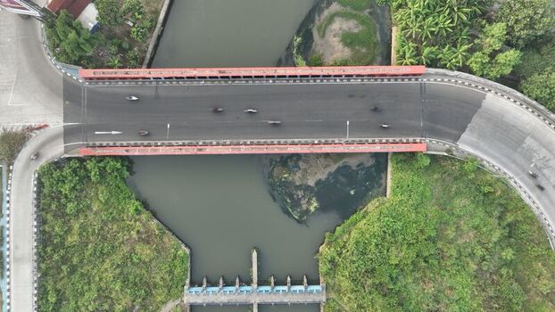 Aerial view of a bridge spanning a river with lush green vegetation and road infrastructure in Bekasi Barat West Java Indonesia. Aerial view of a bridge spanning a river with lush green vegetation and road infrastructure in Bekasi Barat West Java Indonesia.