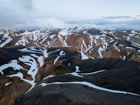 Aerial view of Landmannalaugar featuring colorful rhyolite mountains with patches of snow and dark volcanic soil under a cloudy sky in Rangarthing ytra Iceland. Aerial view of Landmannalaugar featuring colorful rhyolite mountains with patches of snow and dark volcanic soil under a cloudy sky in Rangarthing ytra Iceland.