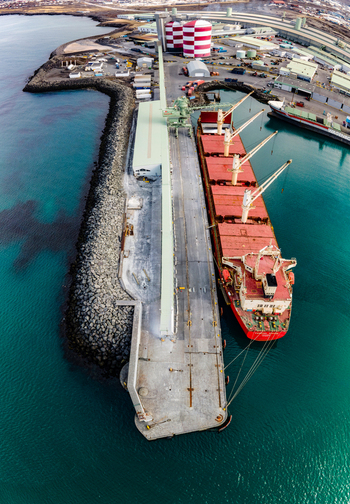 Aerial view of a large cargo ship docked at an industrial port with red and white striped silos and turquoise water in Hafnarfjordur Hafnarfjardarkaupstad Iceland. Aerial view of a large cargo ship docked at an industrial port with red and white striped silos and turquoise water in Hafnarfjordur Hafnarfjardarkaupstad Iceland.