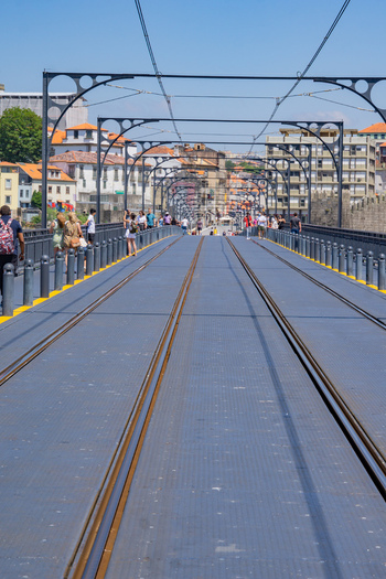 View of the Dom Luís I Bridge with its intricate metalwork casting shadows on the walkway as pedestrians stroll across it Porto Porto District Portugal. View of the Dom Luís I Bridge with its intricate metalwork casting shadows on the walkway as pedestrians stroll across it Porto Porto District Portugal.