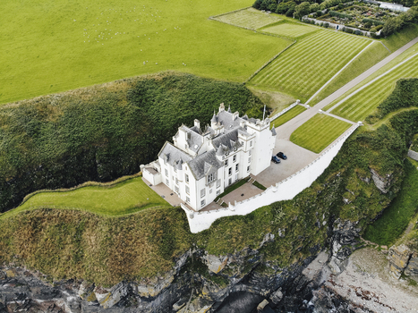 Aerial view of Dunbeath Castle perched on rugged cliffs overlooking the sea with manicured lawns and gardens in Dunbeath Scotland United Kingdom. Aerial view of Dunbeath Castle perched on rugged cliffs overlooking the sea with manicured lawns and gardens in Dunbeath Scotland United Kingdom.