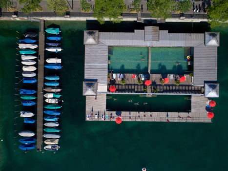 Aerial view of the Frauenbad Stadthausquai public bath with people swimming red umbrellas on the wooden deck and a pier with moored boats in the Limmat river in Zurich Zurich Switzerland. Aerial view of the Frauenbad Stadthausquai public bath with people swimming red umbrellas on the wooden deck and a pier with moored boats in the Limmat river in Zurich Zurich Switzerland.