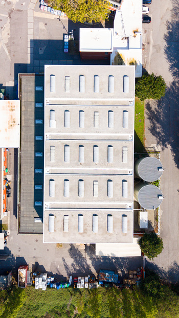 Aerial view of an industrial building with a flat roof featuring multiple skylights adjacent storage tanks and surrounding paved areas in Milan Lombardy Italy.
