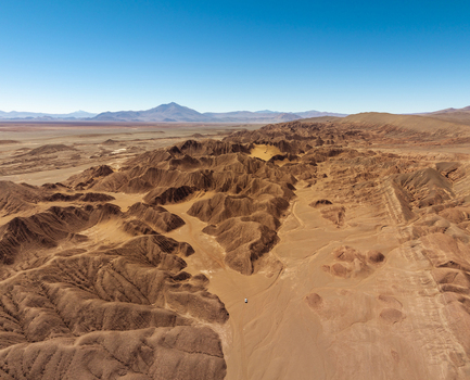 Aerial view of the rugged desert landscape of Tolar Grande featuring deep canyons undulating sand dunes and distant mountains under a clear blue sky in Tolar Grande Salta Province Argentina. Aerial view of the rugged desert landscape of Tolar Grande featuring deep canyons undulating sand dunes and distant mountains under a clear blue sky in Tolar Grande Salta Province Argentina.